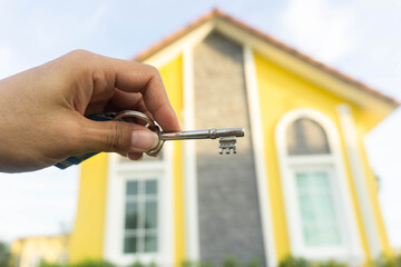 Woman's hand was holding a key and there was yellow house as the background.