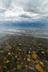 Baikal transparent water with pebbles under and reflection of clouds