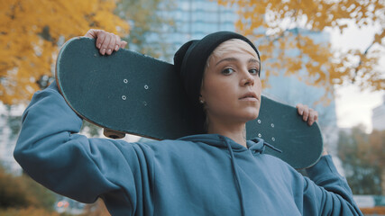 Young caucasian confident woman skater holding skateboard behind her head in the park in autumn. High quality photo