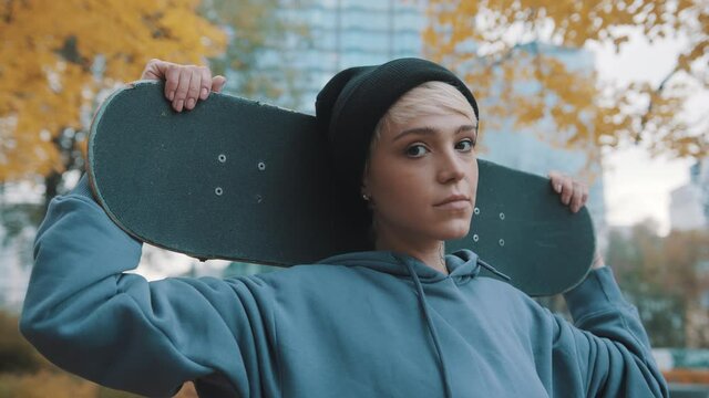 Young blond caucasian woman skater holding skateboard behind her head in the park in autumn. High quality 4k footage