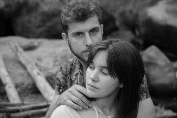 Obraz premium Serious couple sit on wooden footbridge between rocks over stream. Boyfriend flirts with girlfriend, she pretends to ignore. Happiness in relationships. Beautiful natural black and white matte tones.