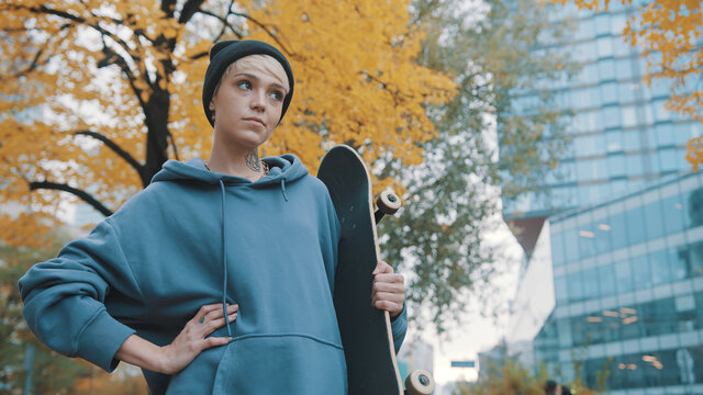 Rebellious teenager, girl, holding the scateboard in the city park in autumn. High quality photo