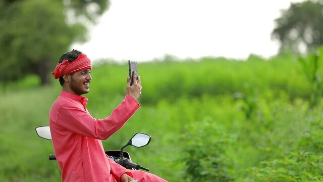 Happy Young indian farmer sitting two wheeler and take selfie at field