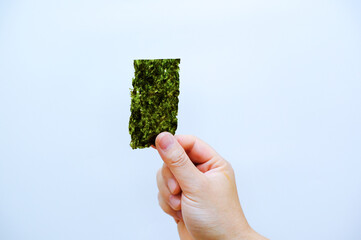 Close-up view of the hand holding a piece of roasted seaweed sheet isolated on white background with copy space. Dry nori sheets korean or japanese for sushi