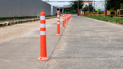 Orange traffic poles on a concrete road. Plastic poles for dividing traffic lines are lined up on the concrete road to warn you of traffic on the road with a copy area. Selective focus
