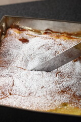 Slicing Karpatka in baking pan. Traditional Polish Cream Pie filled with pudding cream.