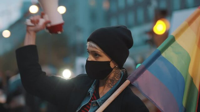 Woman with face mask holding megaphone and rainbow flag. Demonstration against dicrimination . High quality 4k footage