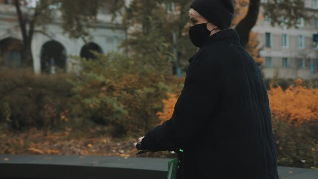 Young woman in winter black jacket with hat and face mask riding electic scooter in the city in autumn. High quality 4k footage