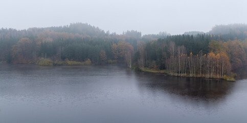 Czech autumn foliage trees landscape on Rimov dam in misty fog