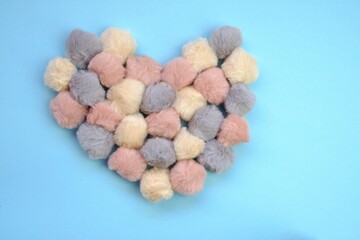 Fototapeta na wymiar Valentine's Day holiday. Heart made of fluffy pom-poms on a blue background. Valentine's day card in pastel colors. Symbol of love, family and fidelity