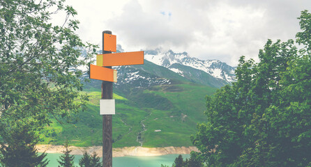 Blank outside sign on the blue lake and green mountains background. Board pointing directions with a blank signpost for your text.