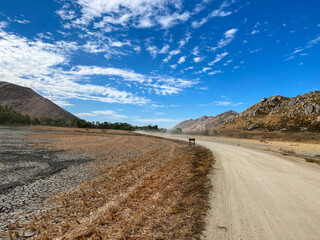 Dusty road curving elegantly in the San Jacinto Wildlife area near Perris, California on a beautiful blue sky day with some clouds. 
