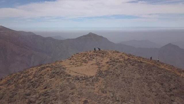 Aerial drone view of people hiking on a hill on a cloudy day and reaching the top. Trekking  in La Vertical Atrapanieblas, La Molina, Lima, Peru.