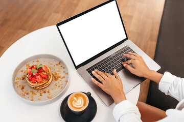women hands at table with laptop near delicious pancakes with berries for breakfast