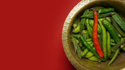 Brass vessel with Green vegetables and red chilly on red background.