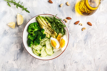 Avocado salad with boiled eggs, broccoli, cucumber, arugula and almond nuts in bowl, Delicious breakfast or snack on a light background, top view