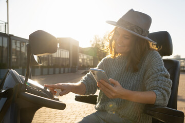 Woman tourist with smartphone on a four wheel mobility electric scooter on a city street.	