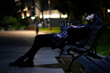 Young lonely woman sitting on a bench at night - 390781970