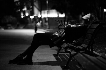 Young lonely woman sitting on a bench at night - 390781993