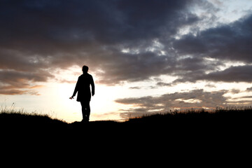 silhouette of a girl standing with a flower in her hands on a background of sunset