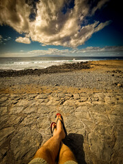Tourist have relax on the coast looking ocean and blue sky in legs pov - concept of summer holiday vacation for people enjoying the amazing view of sea waves and clouds