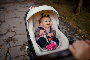 baby girl is sitting in a stroller and smiling during the autumn walk in the park
