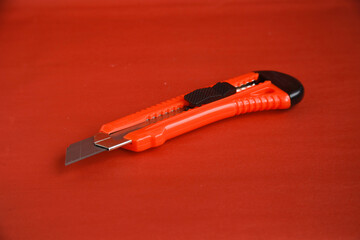 Red cutter knife on red background, sharp knife stationery