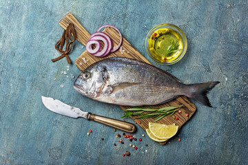 Fresh fish dorada or gilt-head bream on cutting board with spices, olive oil and lemon