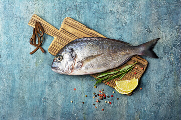 Fresh fish dorada or gilt-head bream on cutting board with spices and lemon