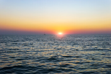 Sailboat silhouetted against a colorful orange sunset sky in the open sea