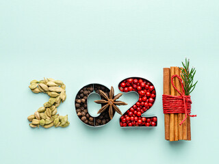 2021 concept. New year 2021 numbers made of spices (cardamom seeds, black peppers, red or pink pepper, anise star and sinnamon sticks wrapped with knit). Mint paper background. Top view. Copy space.