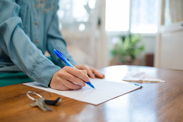 World day of the lease. A woman signs documents, keys are on the table. Hands close-up. Rent and...