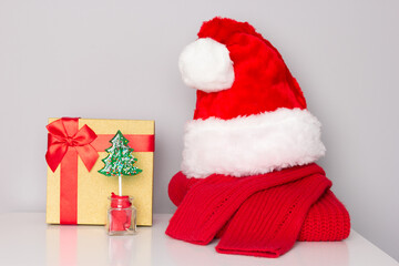 Obraz na płótnie Canvas Santa hat, Christmas sweater, Christmas tree candy, gift box on white table. Christmas surprise preparations