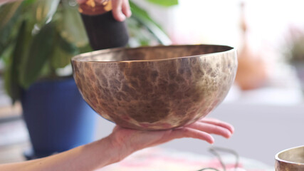 Woman playing on Tibetan singing bowl while sitting on yoga mat. Vintage tonned.