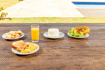 Fototapeta na wymiar Rustiica wooden table, with breakfast. White dishes with toast and eggs, glass of orange juice, fresh cheese and papaya, and green grapes.