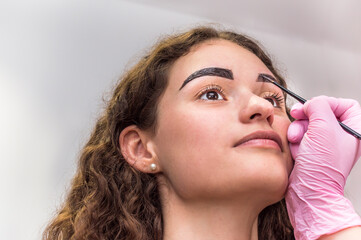 Portrait of young beautiful girl whose eyebrows are plucked. Eyebrow shaping in a beauty salon. Close up of eyebrow and hand of eyebrow artist