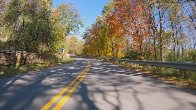 POV Driving a car going up on curvy asphalt Vermont road with colorful trees in fall season. Sunny day with blue sky 