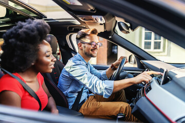 Young cute multicultural couple sitting in a car and preparing for driving.