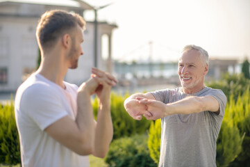 Young bearded male and mature grey-haired male stretching hands outside, talking