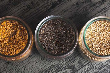 Glass glasses with flax, cia and quinoa seeds photographed from above on a dark background - obrazy, fototapety, plakaty