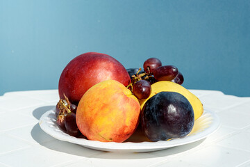 Fresh fruit on a white plate against a blue wall, healthy food concept