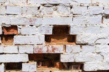 The old brick wall is re-whitewashed with white paint, the brick is already starting to fall out of the wall, an attempt to restore the old wall