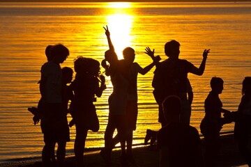 A silhouette of young people having fun on beach at sunset in summer and a cityscape.