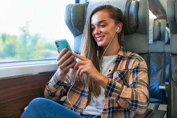 Casual happy young smiling cute woman passenger wearing white headphones using phone for online...