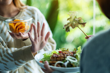 Women choosing to eat potato chips and making hand sign to refuse a vegetables salad