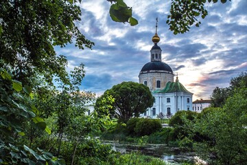 Green trees with bushes and a pond and the Church of the Nativity of the blessed virgin Mary in the background in Vyazma, Russia.