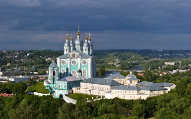 Aerial view on the blue Cathedral of Assumption in a sunny day against dark sky. The cityscape with trees, houses, buildings in summer in Smolensk, Russia.