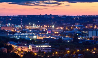 Cityscape of Smolensk in the evening: lit up street lamps among buildings and houses and cloudy pink sky over it in Russia.