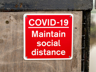 Red and white Covid-19 Maintain social distance sign on a wooden wall