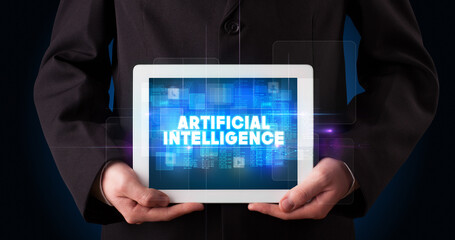 Young business person working on tablet and shows the inscription: ARTIFICIAL INTELLIGENCE